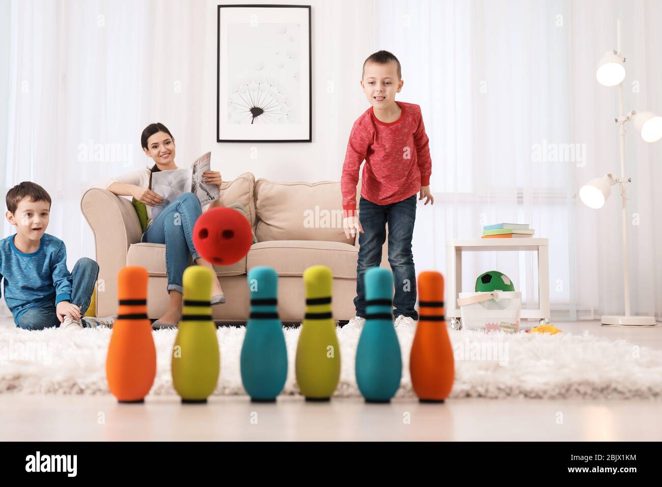 Cute little boys playing bowling while their nanny is reading magazine