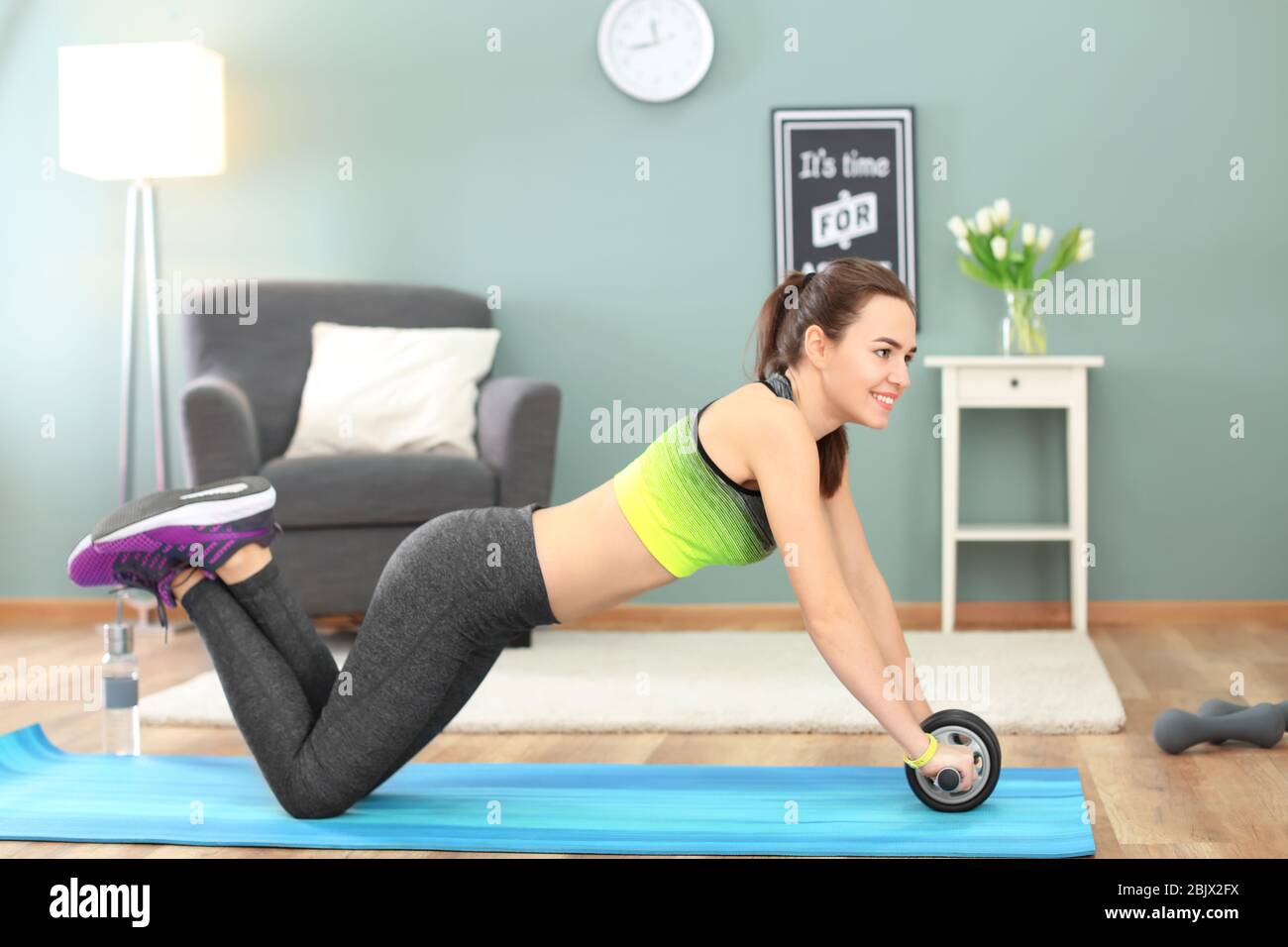 Beautiful young woman doing fitness exercise with roller wheel at home ...