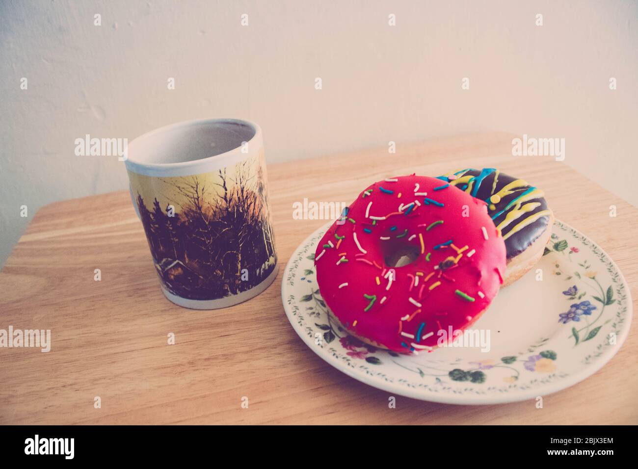 a pair of donuts with a coffee cup in a wood table Stock Photo