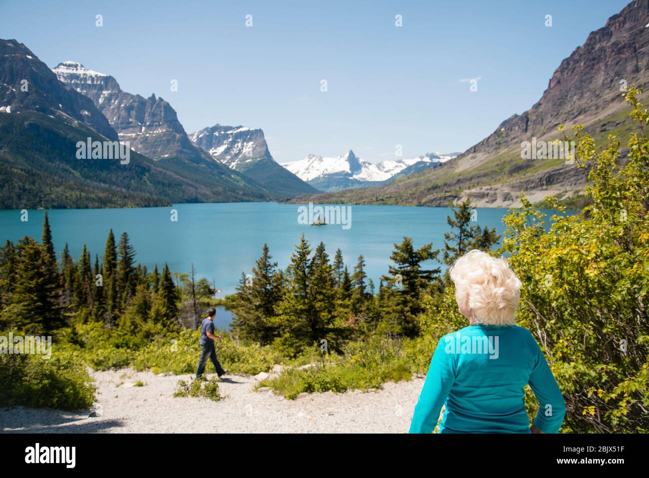 70 year old senior tourist woman looking at mountains, lake scenic view. Enjoying the beauty of nature at Glacier National Park. Copy space background Stock Photo