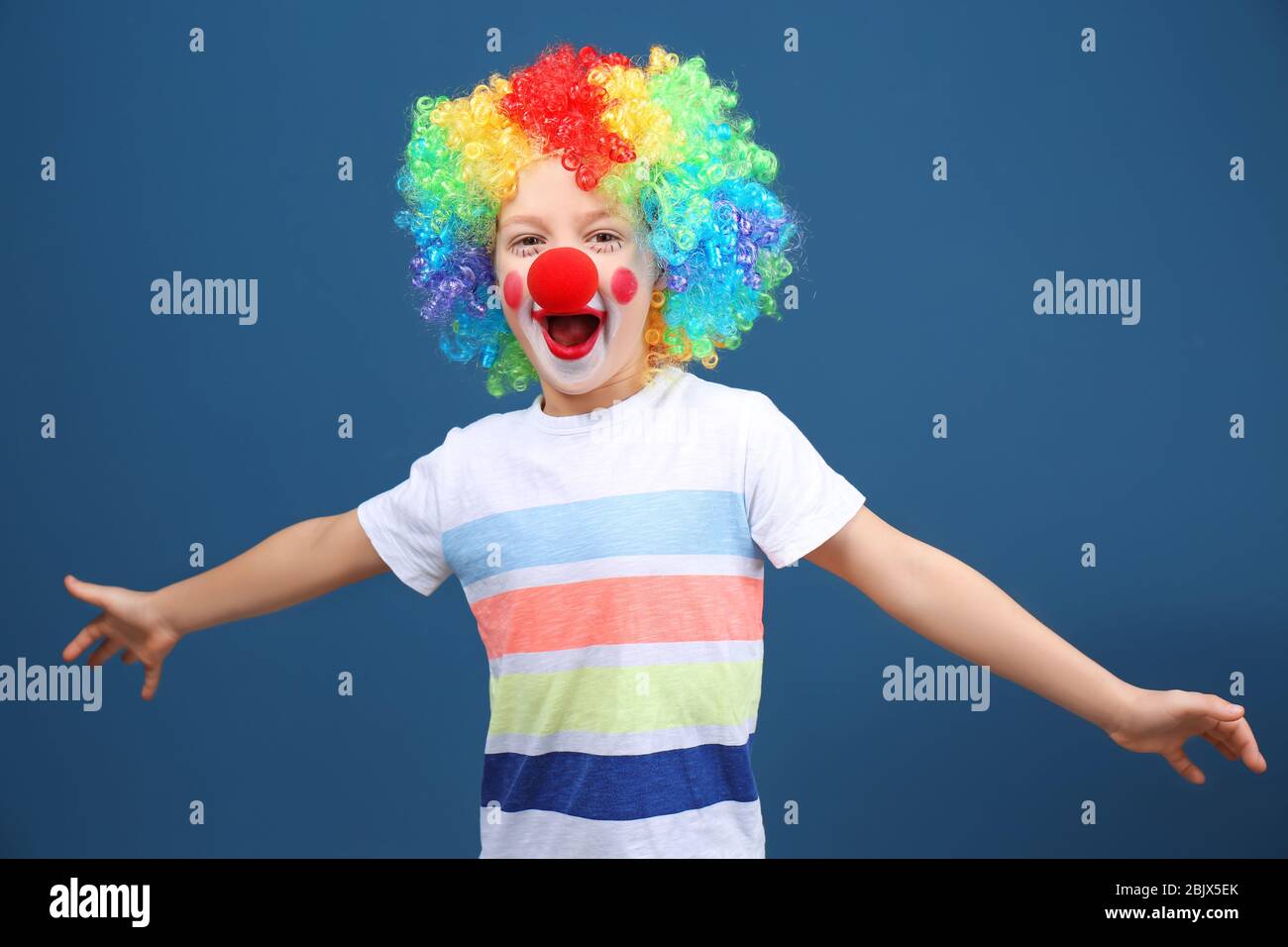 Cute little boy with clown makeup in rainbow wig on color background