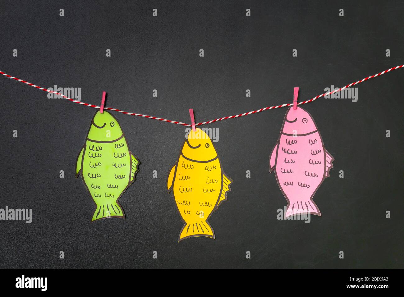 Paper fish hanging on string near chalkboard. April fool's day ...