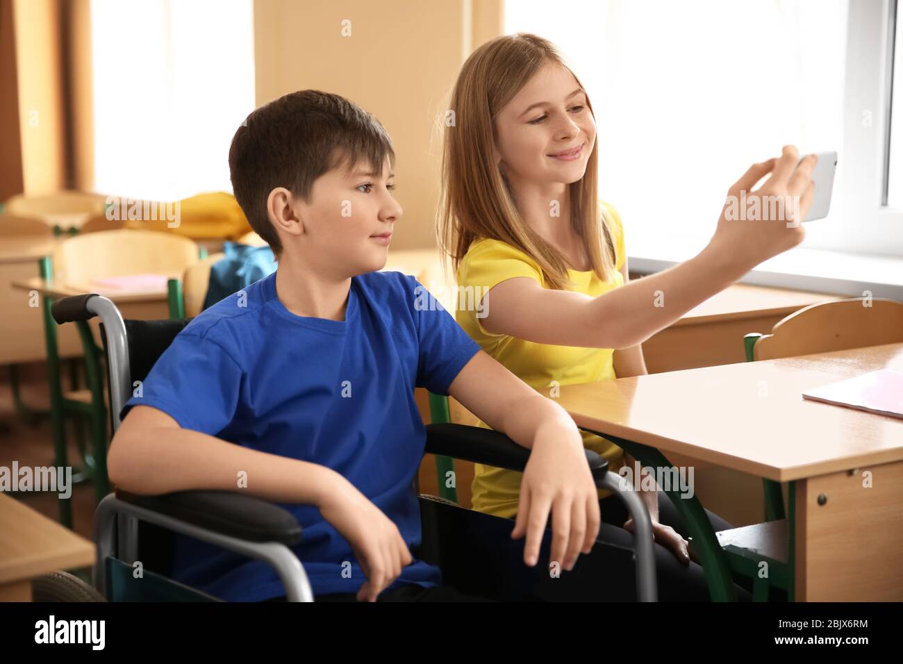 Teenage girl with boy in wheelchair taking selfie at school Stock Photo ...