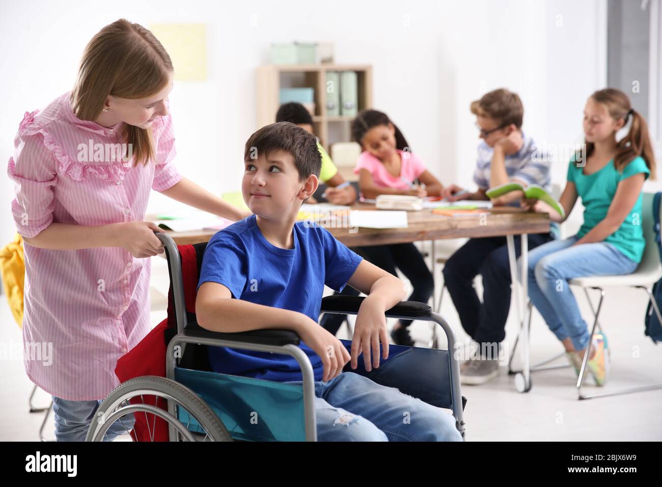 Girl helping boy in wheelchair at school Stock Photo