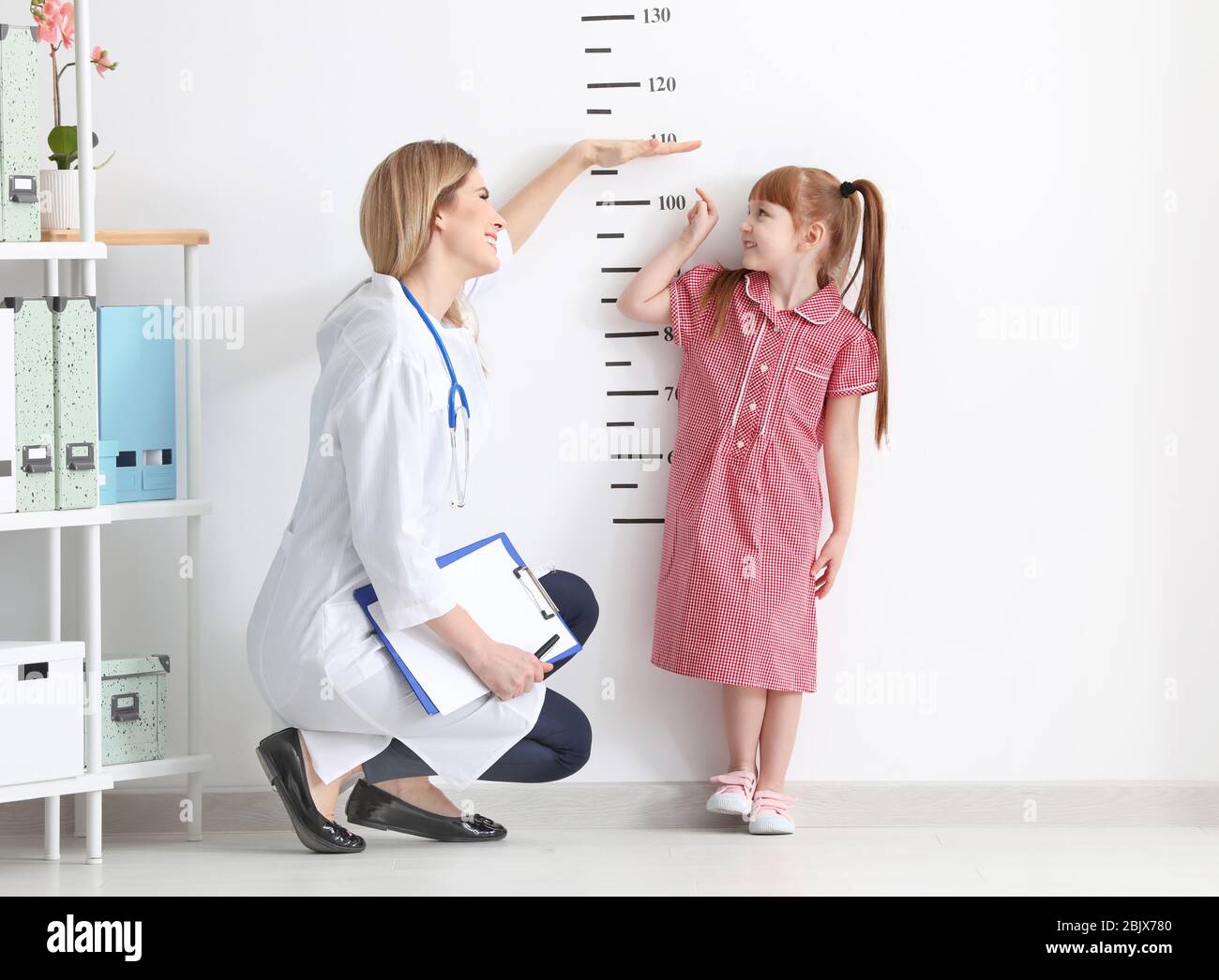 Female doctor measuring height of little girl in clinic Stock Photo
