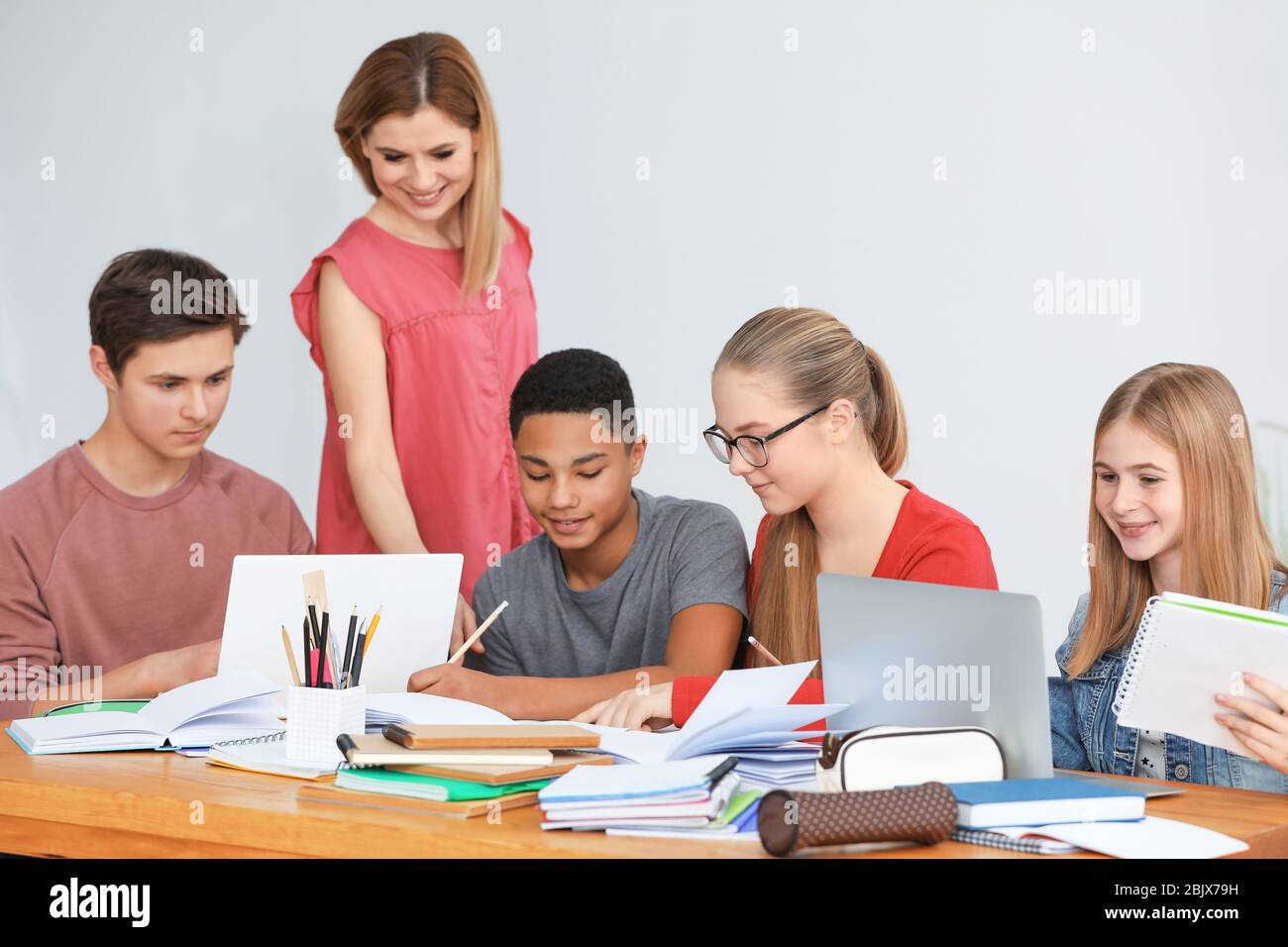 Group of teenagers doing homework with teacher in classroom Stock Photo ...