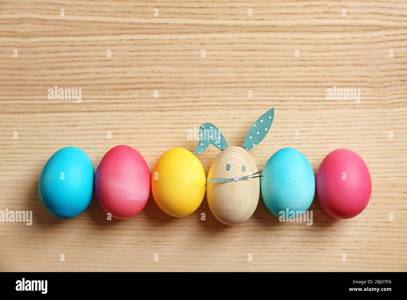 Colorful Easter eggs and one with bunny ears made from paper on wooden ...