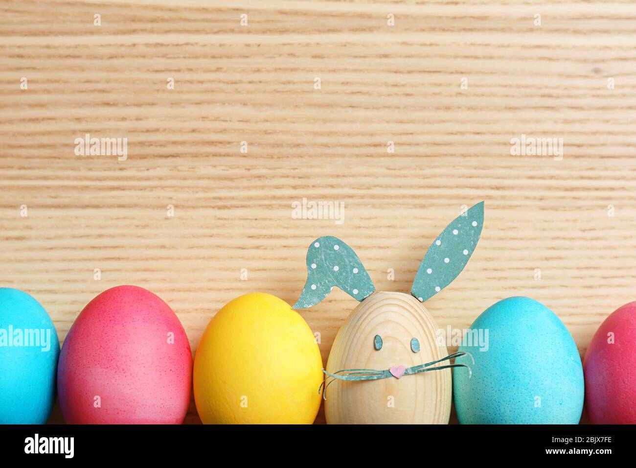 Colorful Easter eggs and one with bunny ears made from paper on wooden ...