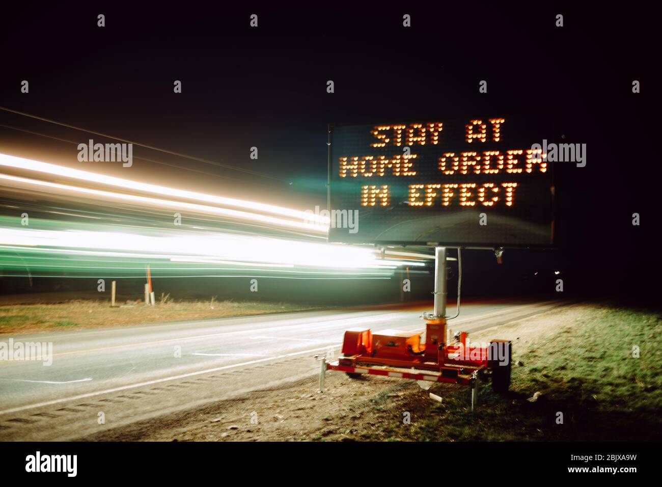Stay at home order in effect displayed on roadside digital sign at night as cars pass by.  Covid-19 pandemic, stay at home order Stock Photo