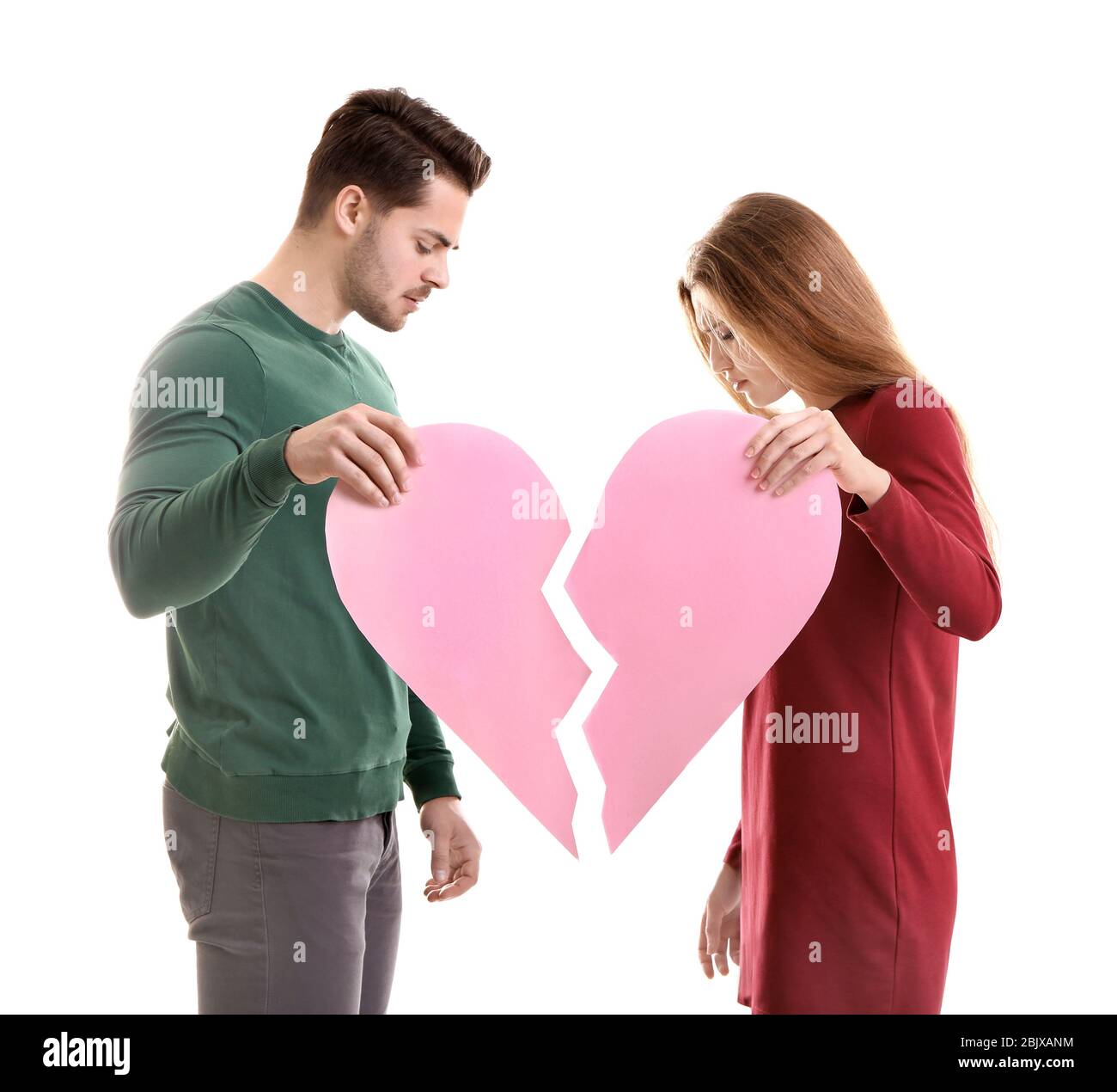 Young couple holding halves of broken heart on white background. Relationship problems Stock Photo
