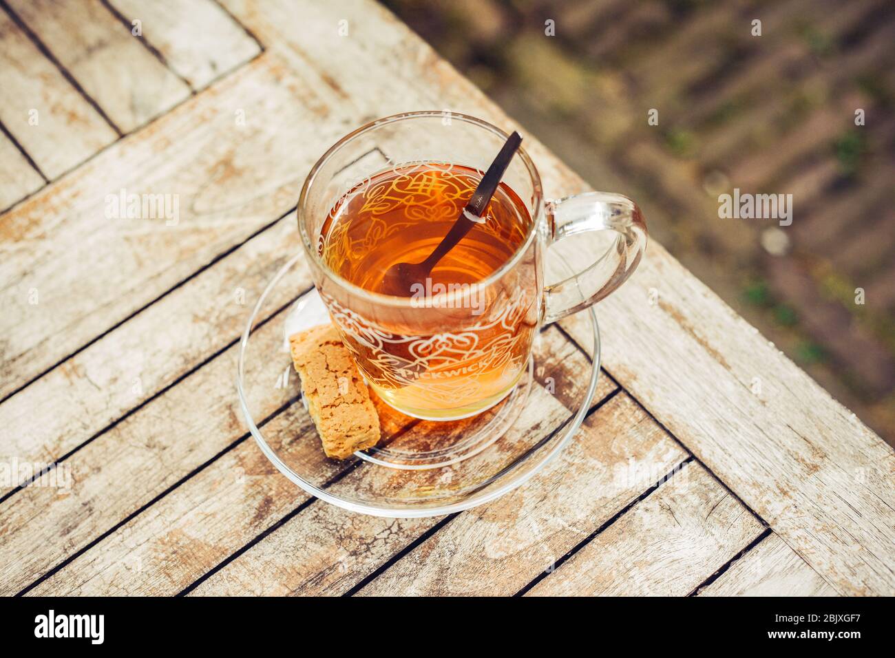 Tea in glass cup on a wooden table outside in the garden. Tea spoon and cookie biscuit. Healthy lifestyle. Background. Wooden pattern. Stock Photo