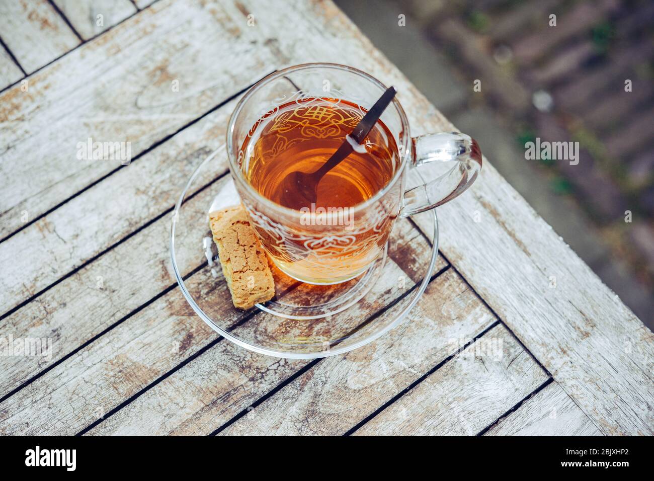 Glass cup of tea on a rustic wooden table outside in the garden. Tea spoon and cookie biscuit. Healthy lifestyle. Stock Photo
