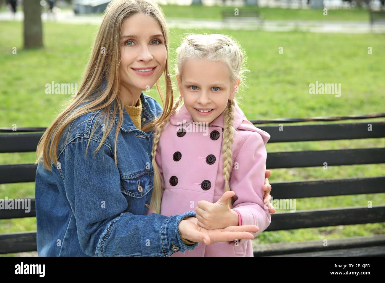 Little deaf mute girl and her mother using sign language outdoors Stock