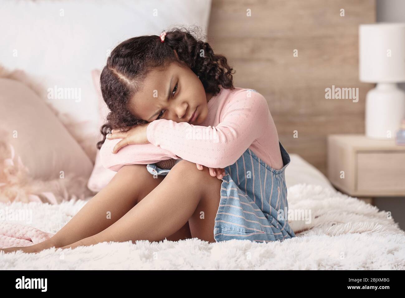 Sad little African-American girl sitting on bed Stock Photo - Alamy