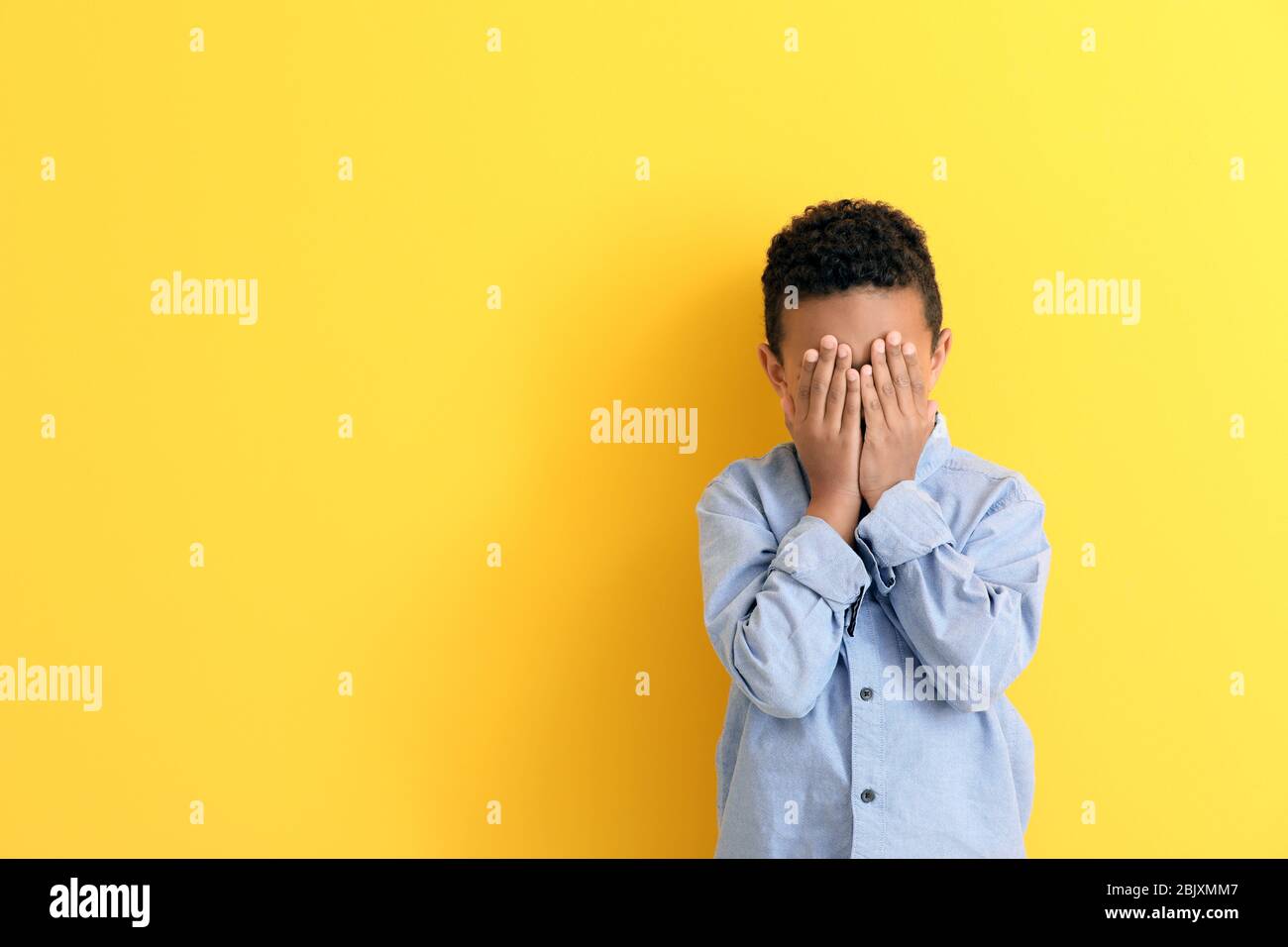 Cute African-American boy covering face with his hands on color ...