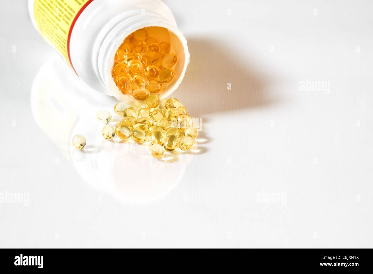Vitamin D3 clear yellow gel capsules spilling from supplement bottle.  White background with reflection and copy space Stock Photo