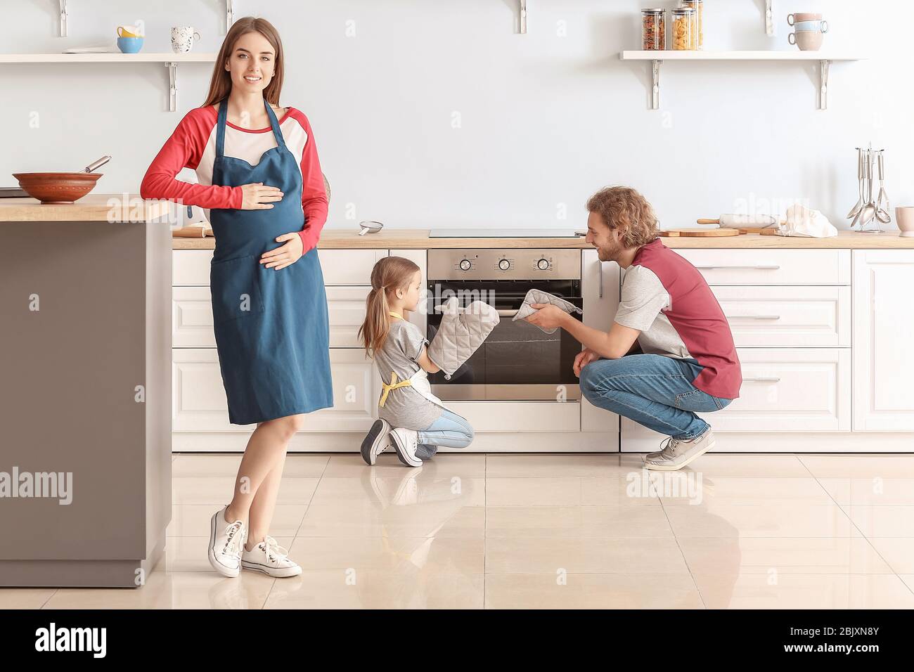 Young pregnant woman and her daughter with husband baking pastry in