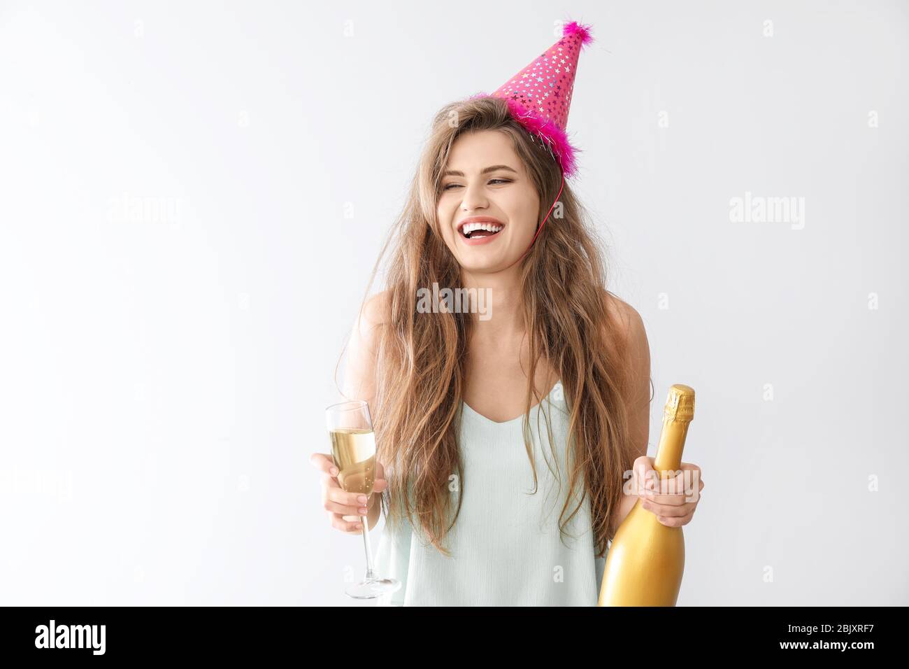 Drunk woman with party hat and champagne on light background Stock ...