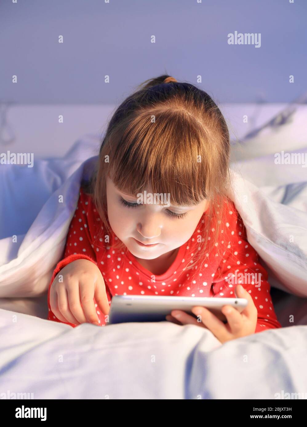 Cute little girl using tablet computer in bed at night Stock Photo - Alamy