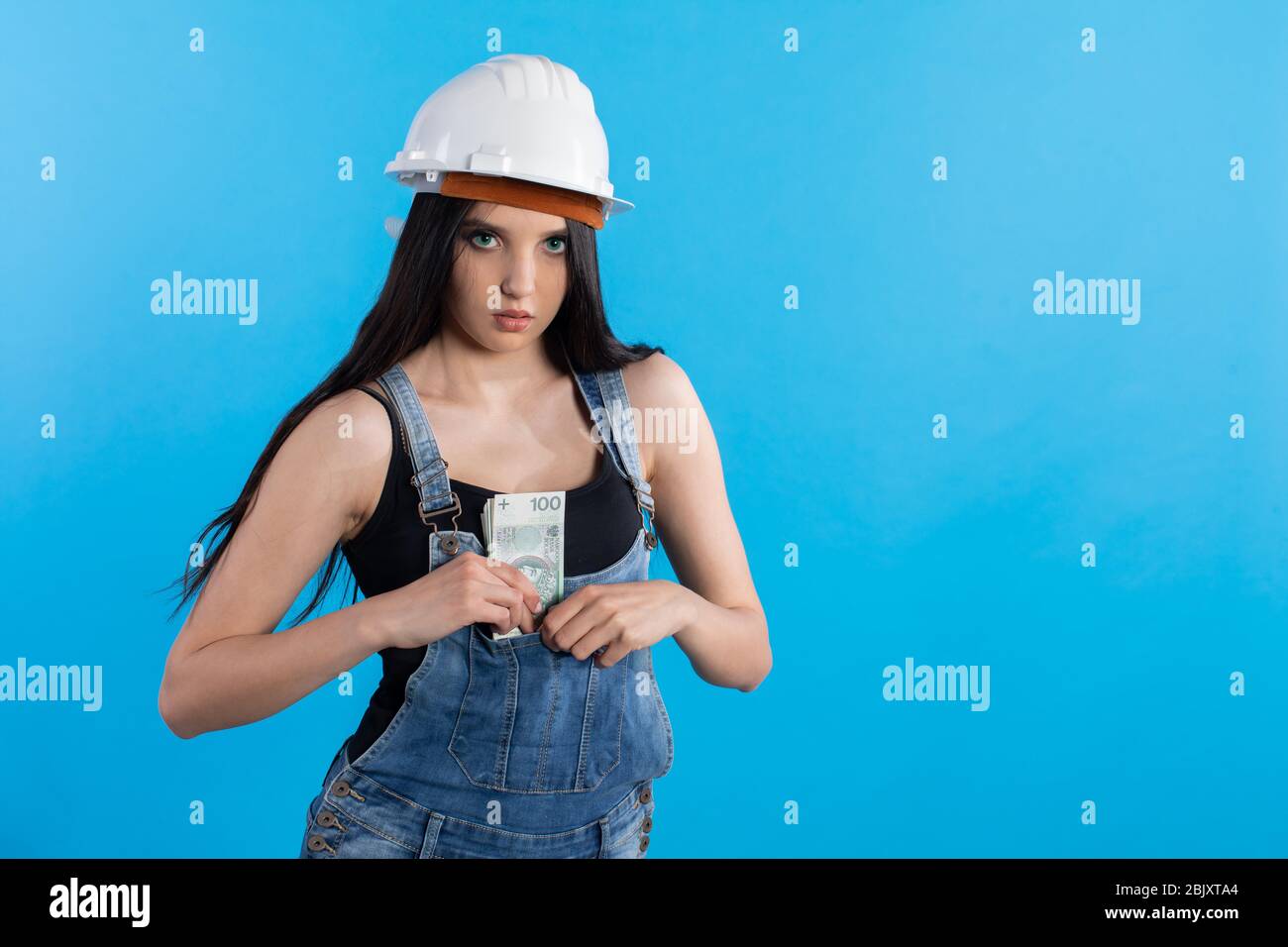 A young female construction worker hides a thick bundle of banknotes in her pants pocket gardeners. Stock Photo