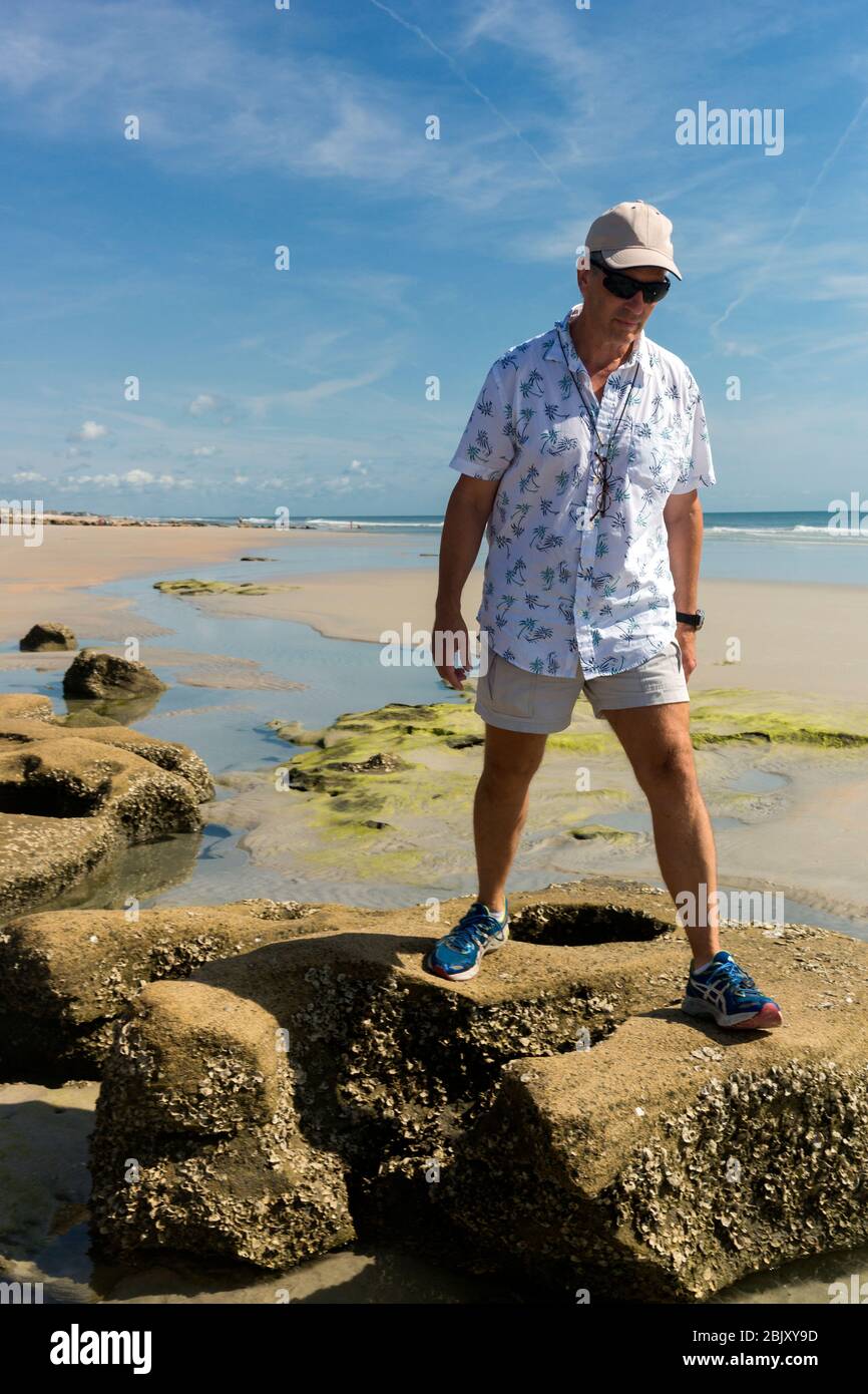 Adult man walks on the beach tidepooling among coquina rock formations on the shore of the Atlantic Ocean, Marineland Beach, St. Augustine, FL Stock Photo