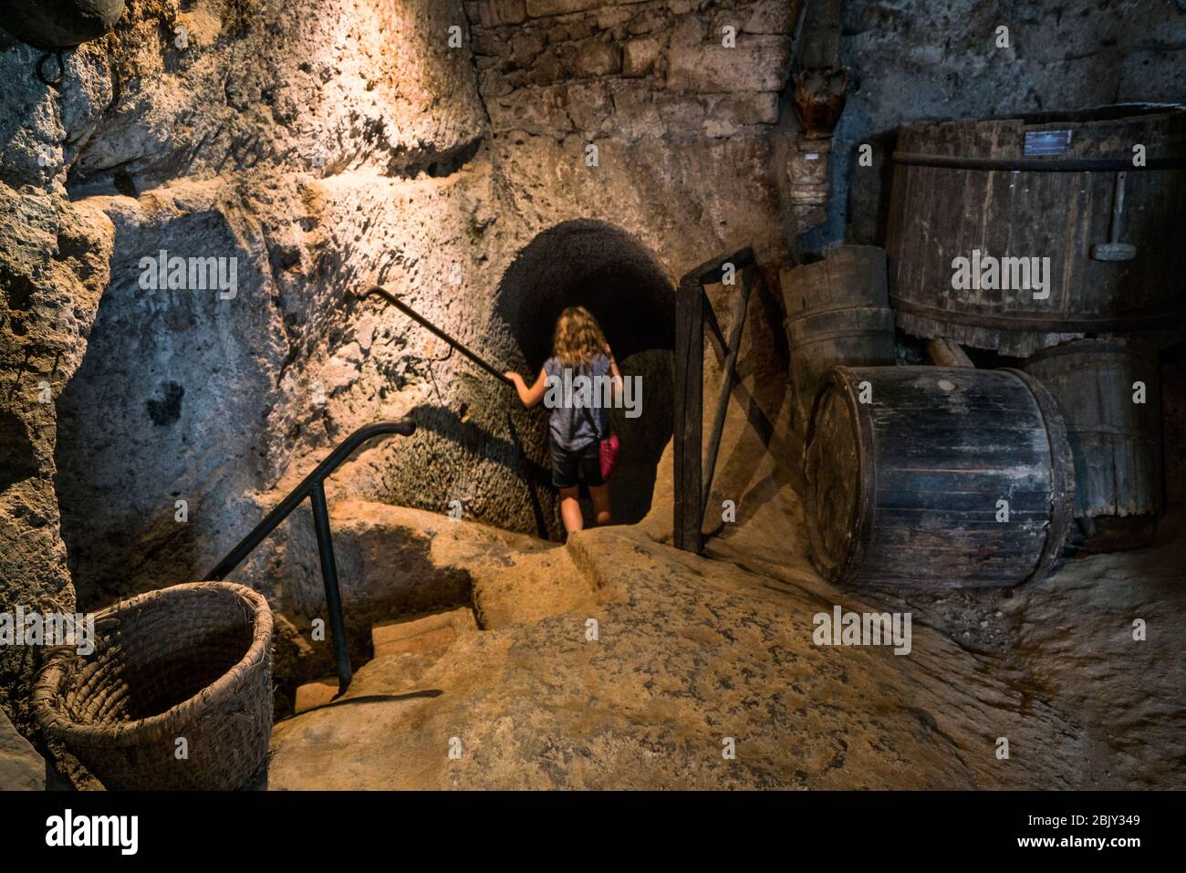 Female tourist descends the dark passageway to the underground wine cellar and olive oil press inside Cività di Bagnoregio, Civita Bagno, Italy Stock Photo