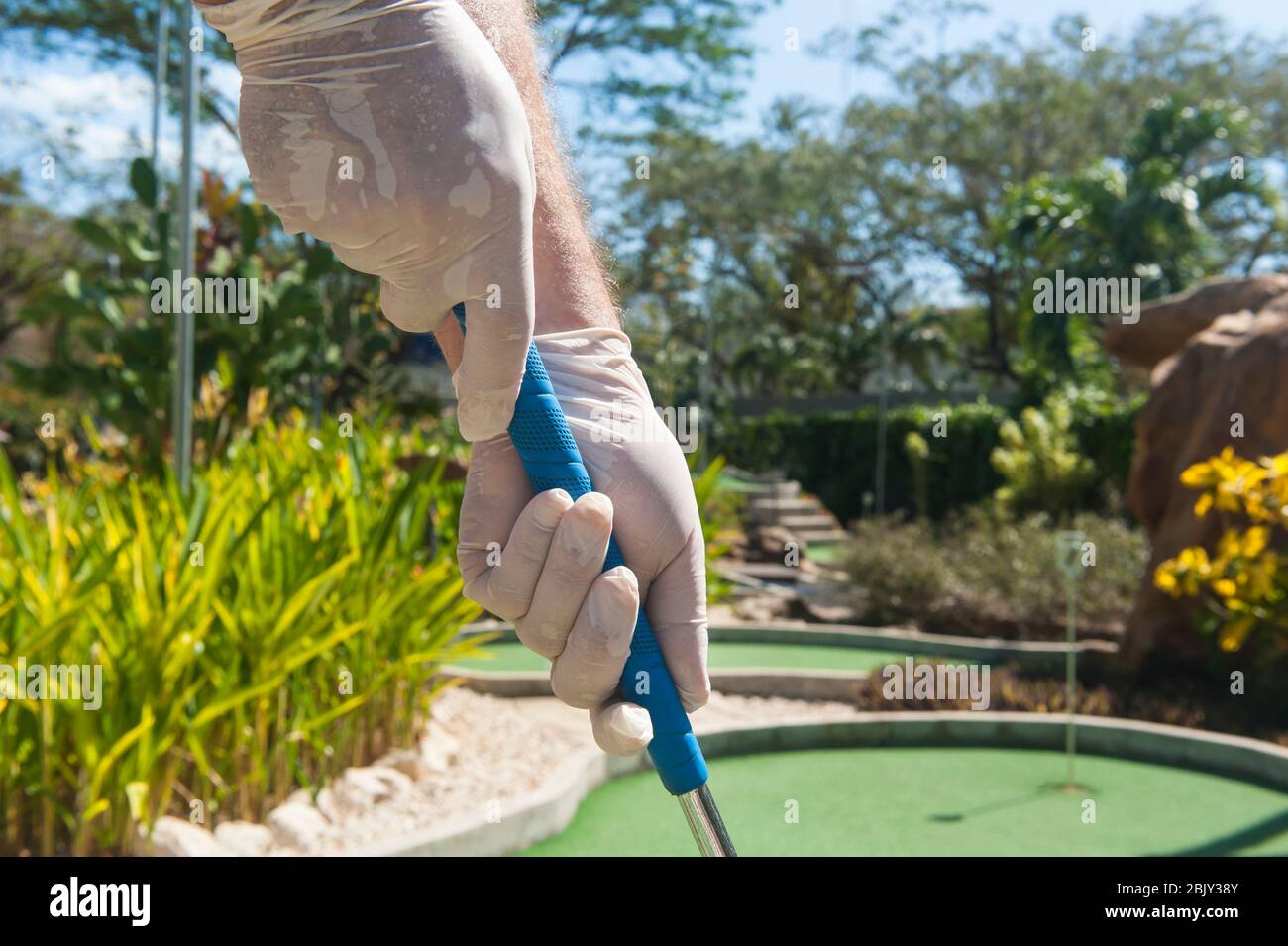 Gloved hands holding a blue mini golf club in the sun Stock Photo