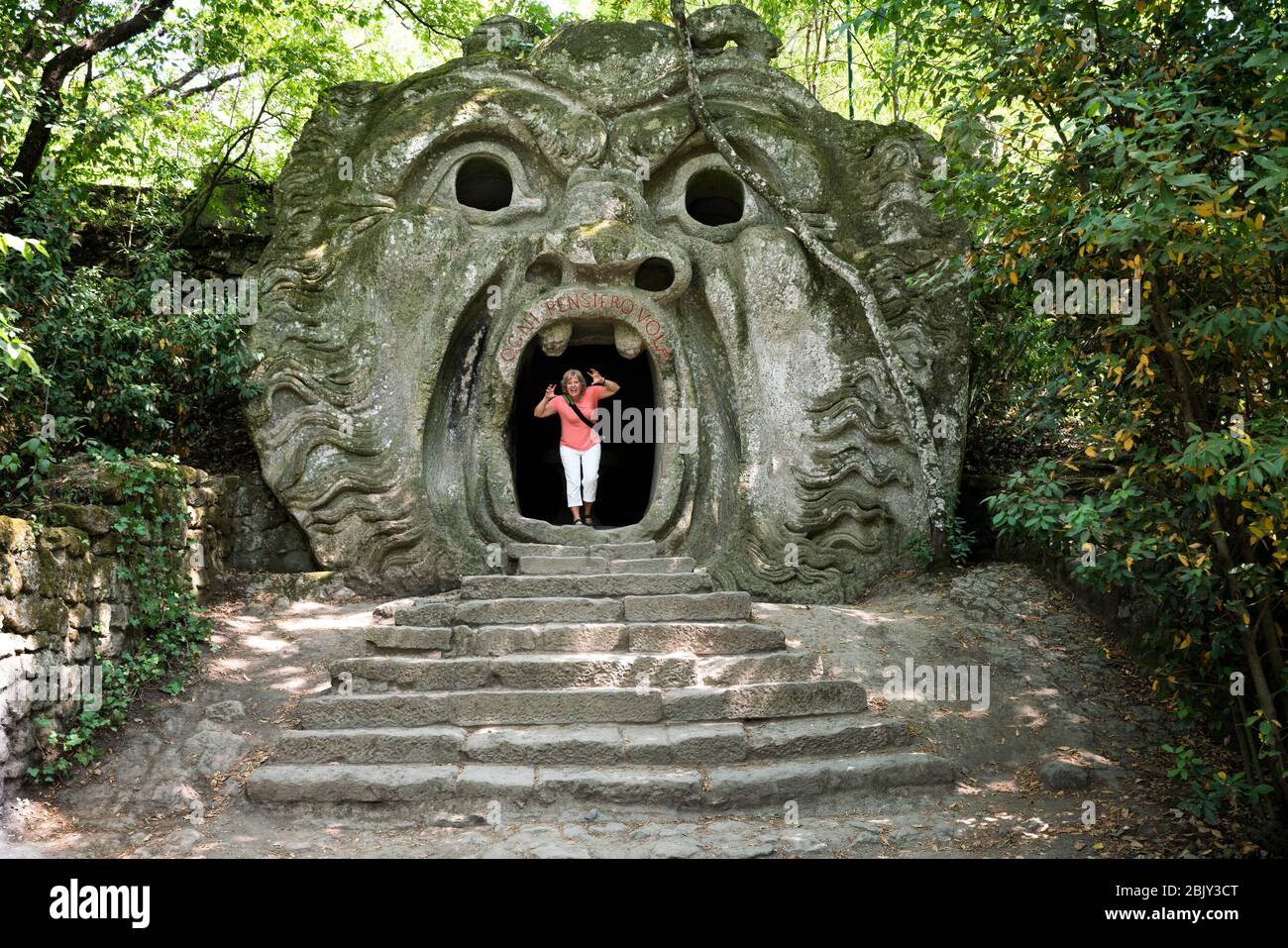 Female tourist makes a scary face standing in the Mouth of Hell at the Monster Park, Parco dei Mostri, that was commissioned in 1552 by Prince Pier Fr Stock Photo