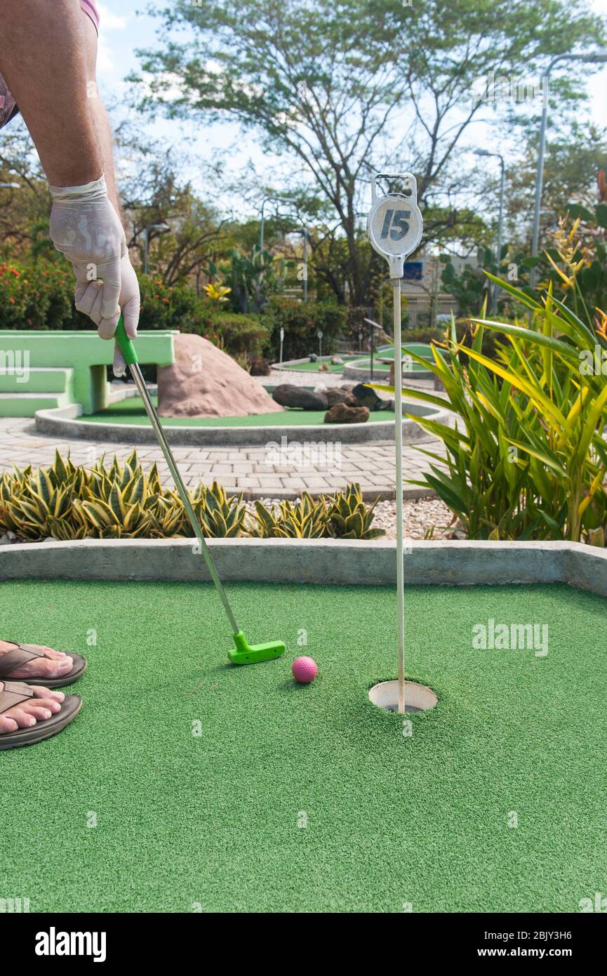 Man making a mini golf putt wearing protective gloves Stock Photo