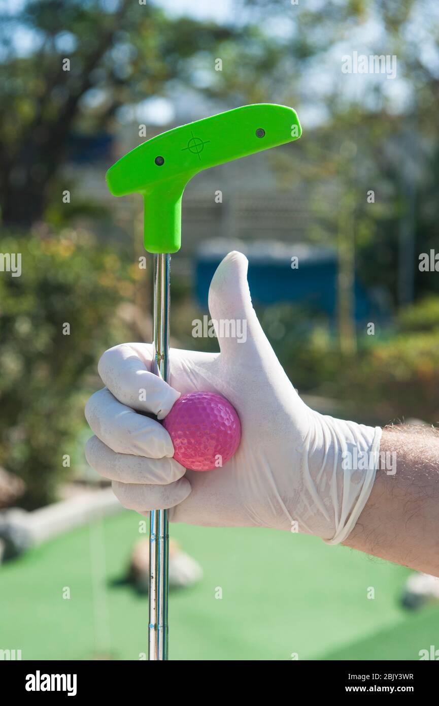 Hand wearing gloves gives the thumbs up sign while holding a mini golf club and ball Stock Photo