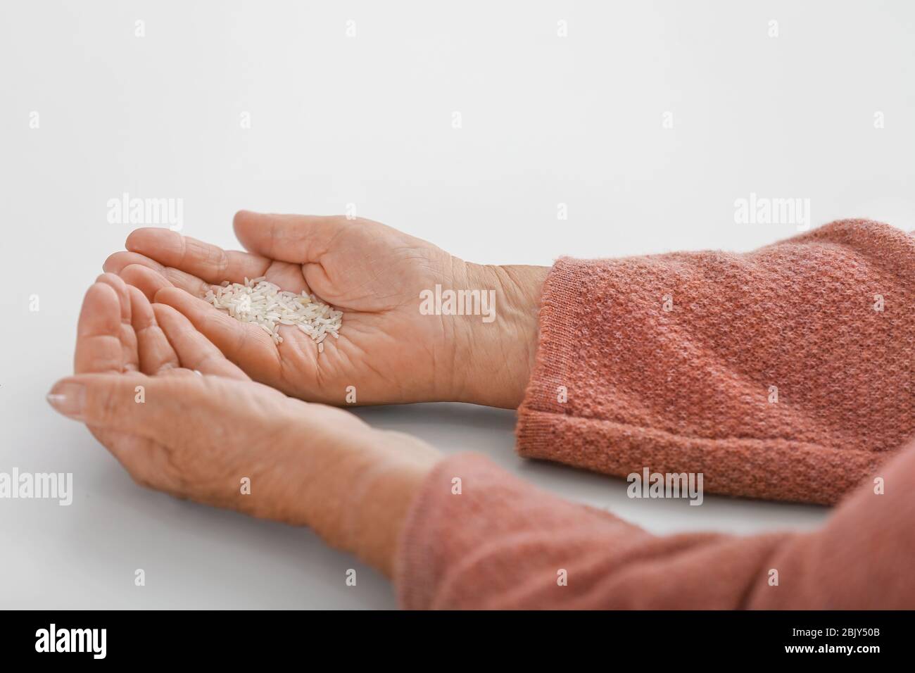 Hands of elderly woman with rice on white background. Concept of poverty Stock Photo