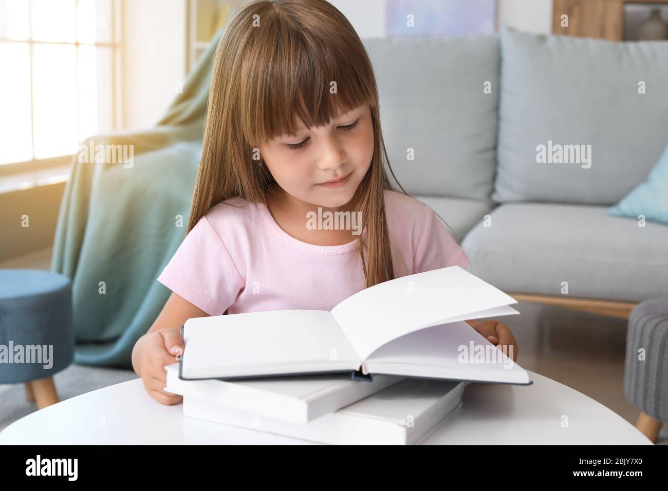 Cute little girl reading book at home Stock Photo - Alamy