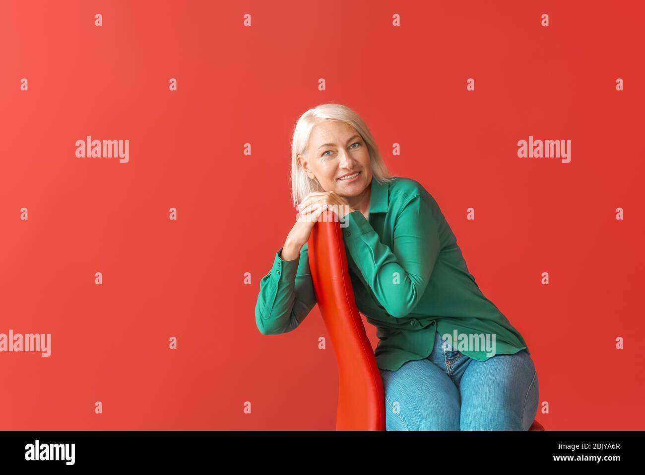 Mature woman sitting on chair against color background Stock Photo - Alamy