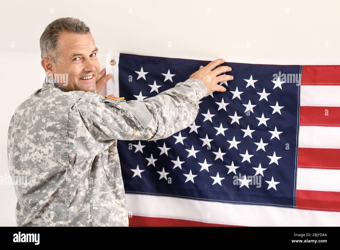 Mature male soldier hanging USA flag on wall in headquarters building ...