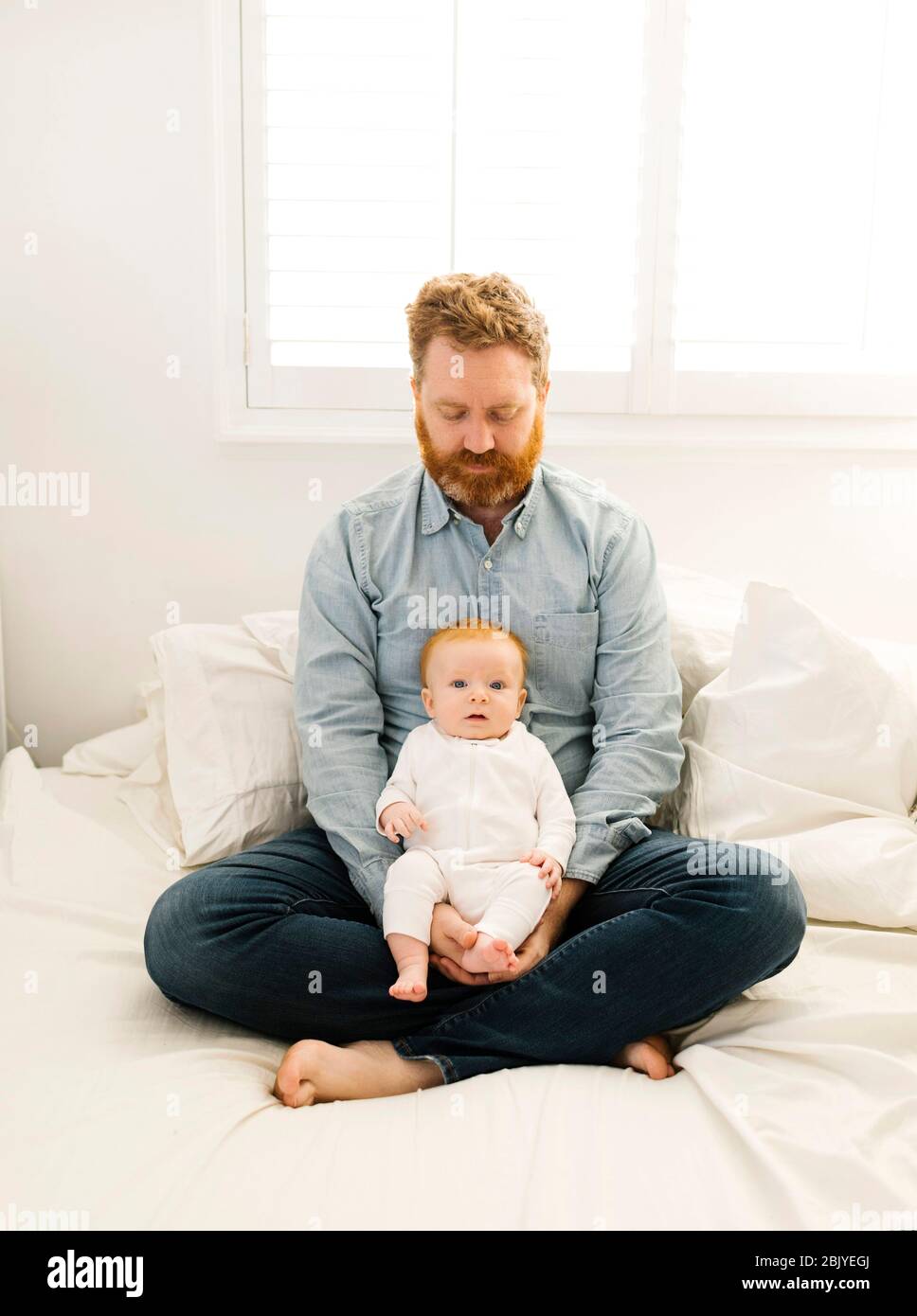 Father sitting on bed with baby boy (2-3 months) Stock Photo