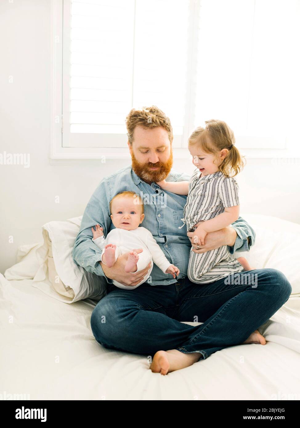 Father sitting on bed with children (2-3 months, 2-3) Stock Photo