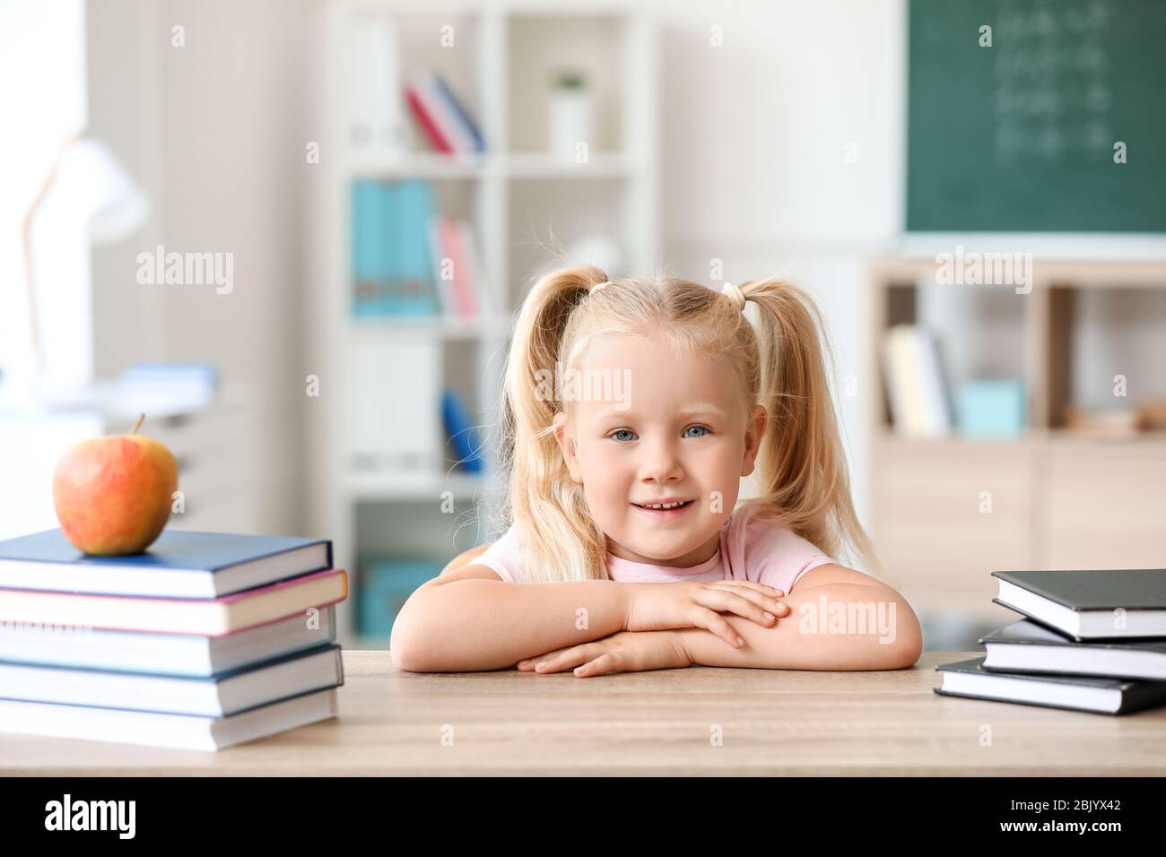 Cute little schoolgirl sitting at desk in classroom Stock Photo - Alamy