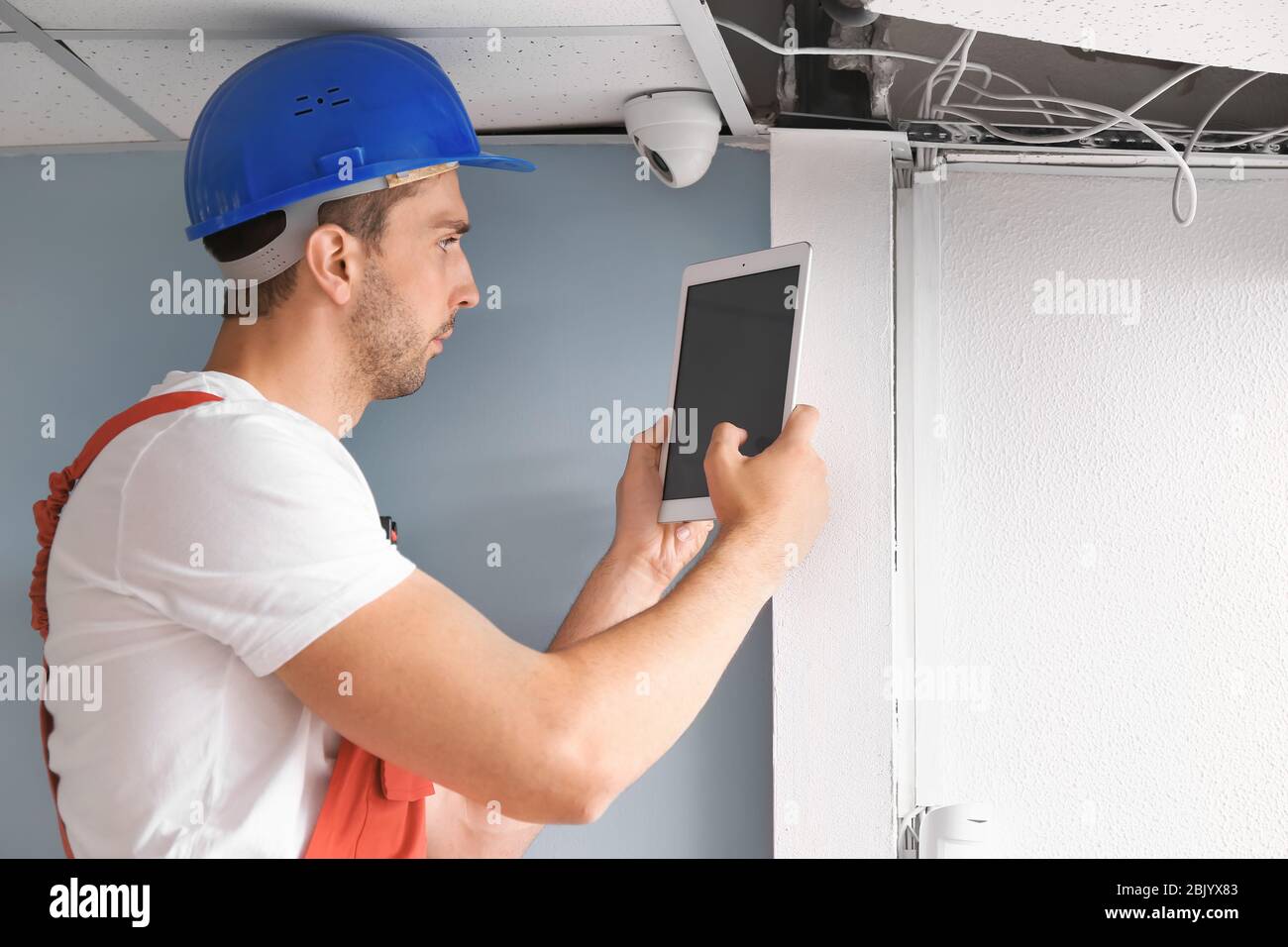 Electrician with tablet computer installing alarm system indoors Stock Photo