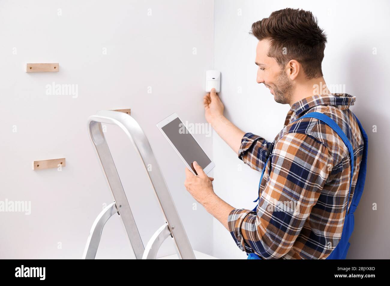 Electrician with tablet computer installing alarm system indoors Stock Photo