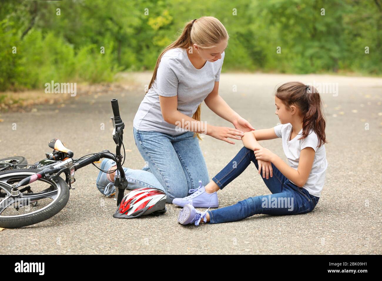 Mother helping her little daughter after falling off bicycle outdoors