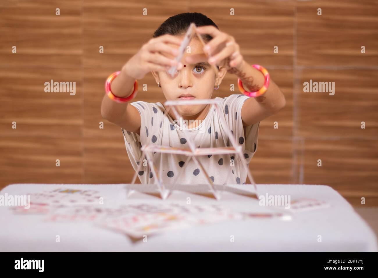 Young girl kid busy in building Pyramid with house of cards at home - concept of focus or concentration excerise game for school children Stock Photo