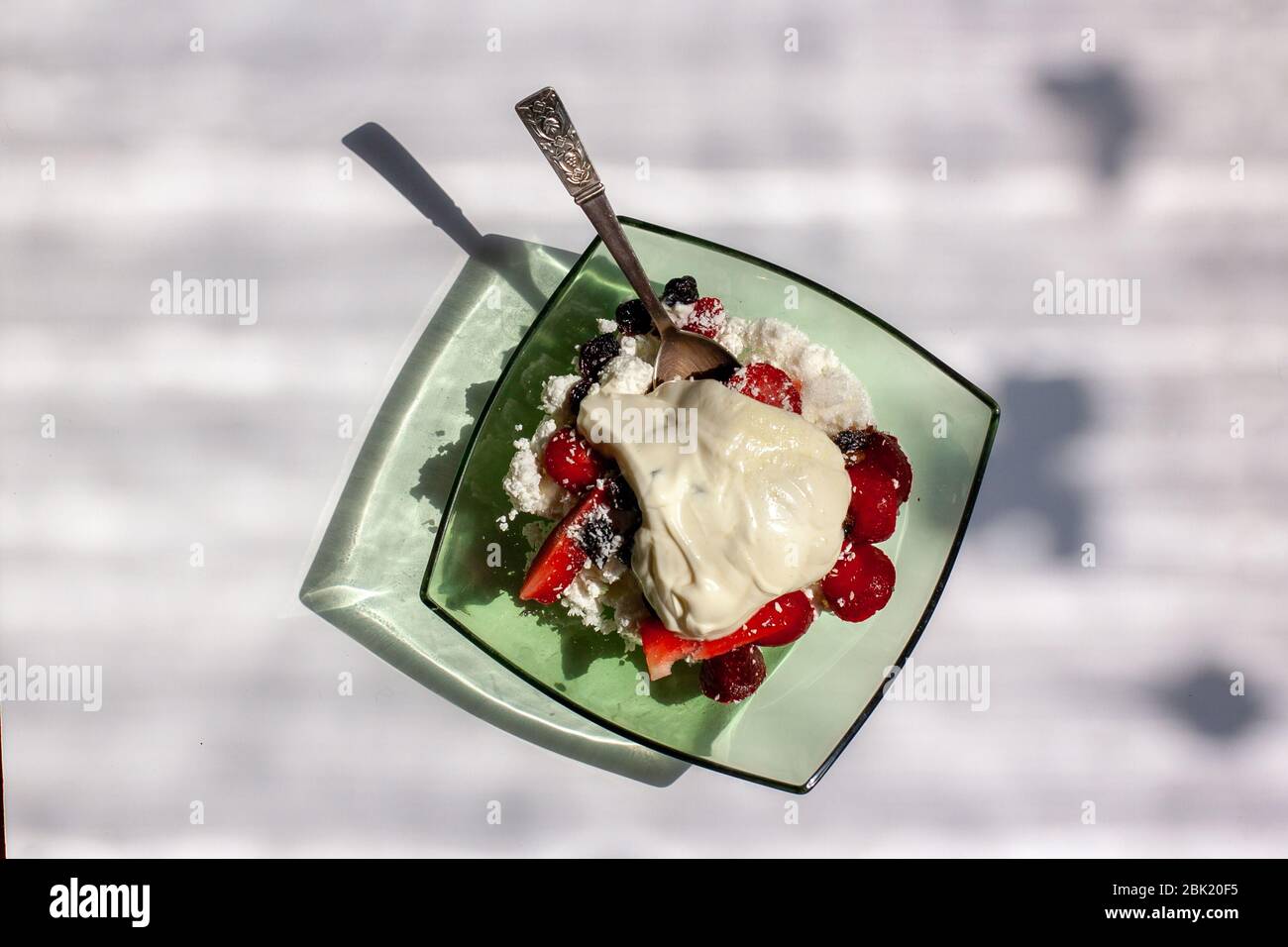 Plate with cottage cheese with sour cream and strawberries with raisins in the style of a flat lay. The glass plate is green. Silver teaspoon inside. Stock Photo