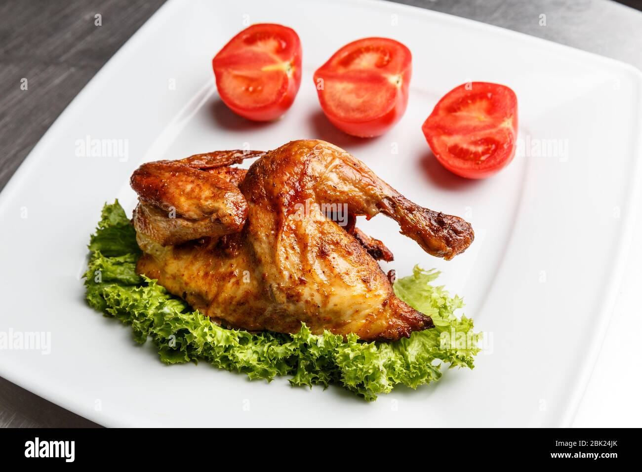 Half of grilled chick served with salad leaves and tomatoes on a white plate in a restaurant Stock Photo