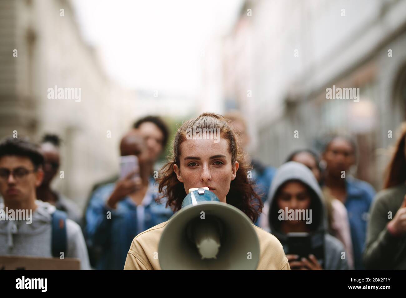 Young woman with a megaphone with group of demonstrator in background. Woman protesting with megaphone in the city. Stock Photo