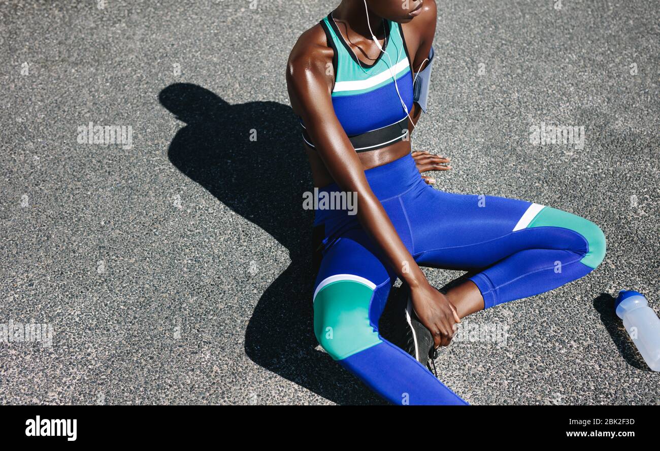 Fitness woman sitting on a road after run. Top view shot of a female in sportswear resting on the road outdoors with a water bottle on the side. Stock Photo