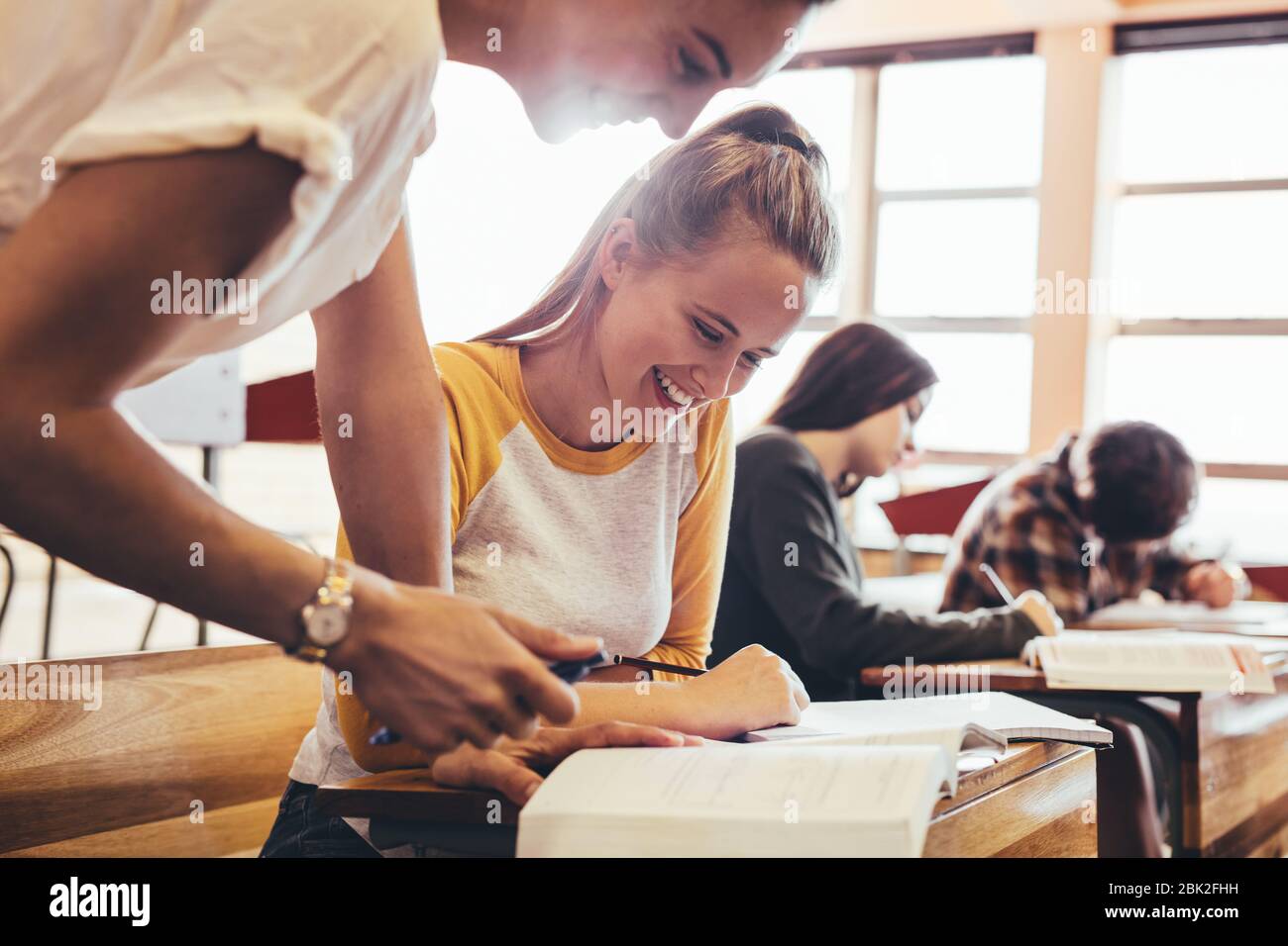 Young woman studying with teacher standing by in classroom. High school teacher helping student in classroom. Stock Photo