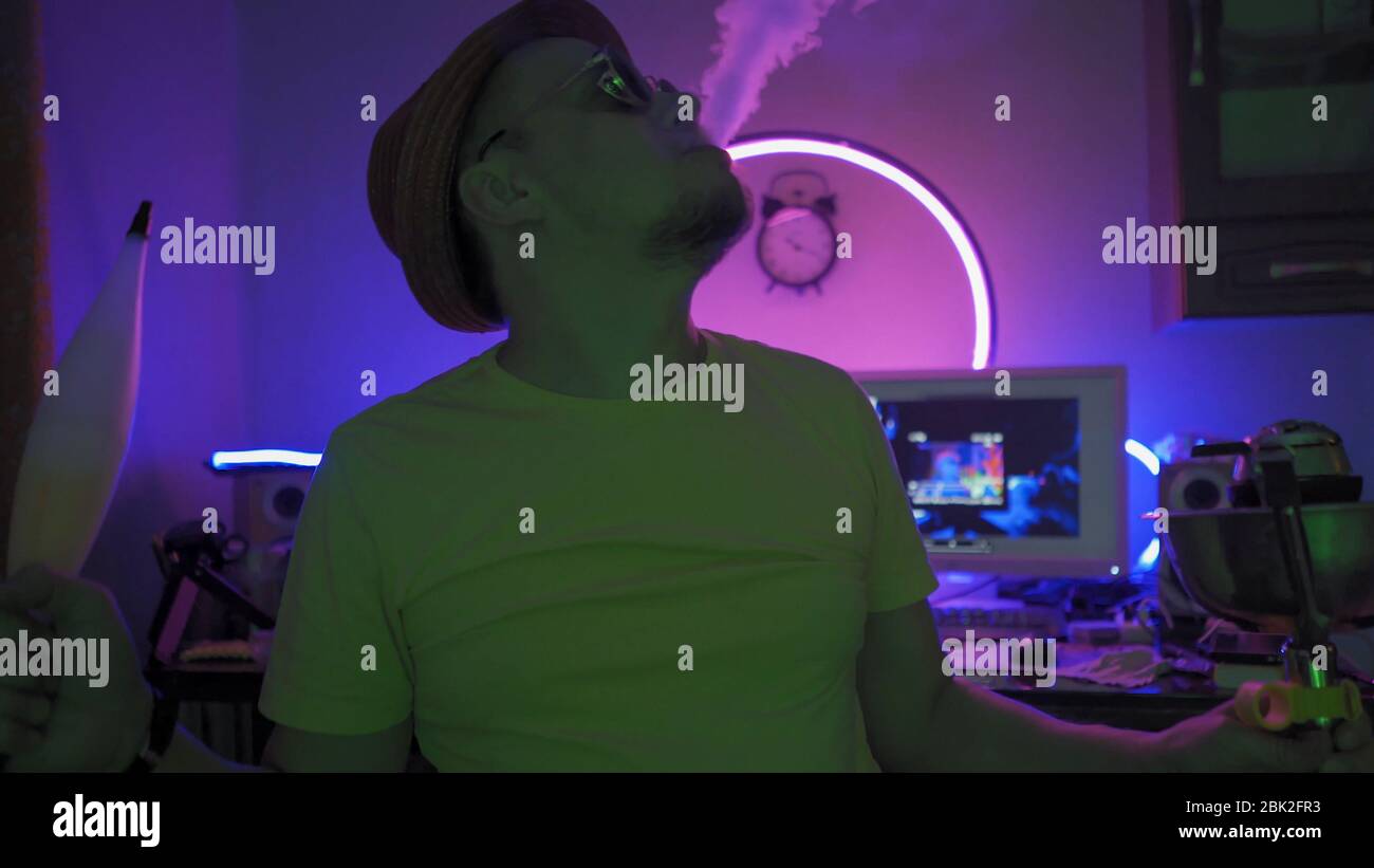 Bearded Man Smokes A Hookah Exhaling Smoke Up In Neon Stock Photo