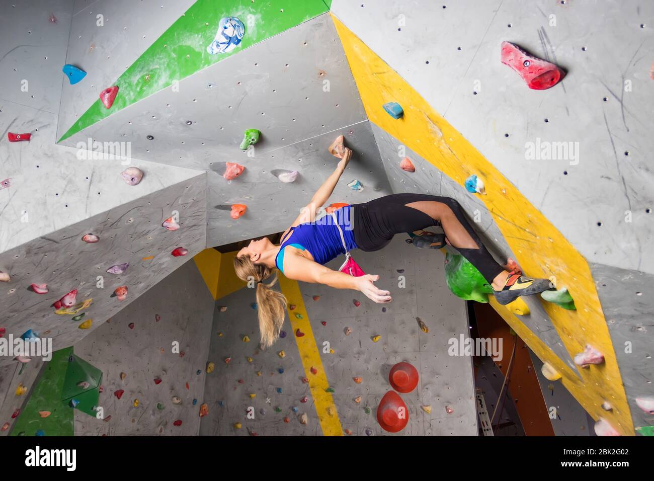 Rock climber woman hanging on a bouldering climbing wall, inside on