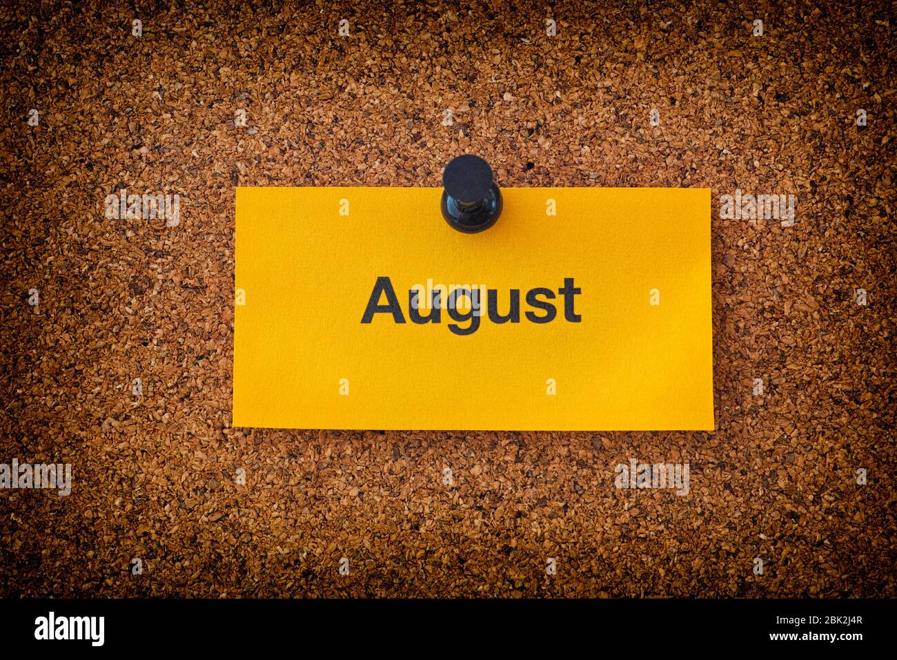 August written on a yellow piece of paper that is on a bulletin board. Close up. Stock Photo