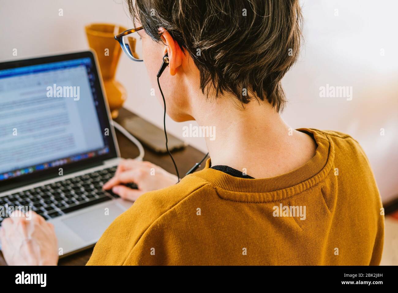 Woman working on desk in home office in old vintage room. Young Caucasian short hair woman with earphones working online from home on computer laptop Stock Photo
